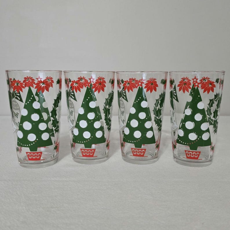 May include: Four clear drinking glasses with Christmas tree designs. Each glass features a green Christmas tree with white dots, red poinsettias, and holly leaves. The glasses have a festive, vintage aesthetic.