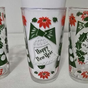 May include: Set of three clear drinking glasses with a festive New Year's design. Each glass features a white background with green bow, red poinsettias, and the text "Happy New Year" in black script. The glasses are ideal for holiday celebrations.
