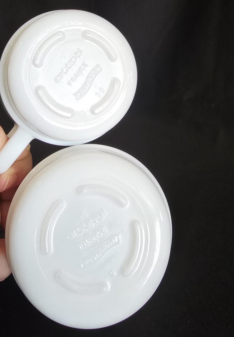 May include: Two white ceramic bowls with a raised rim and a smooth, glossy finish. The bottom of each bowl has the text "Arcopal France" and a logo with a crown.