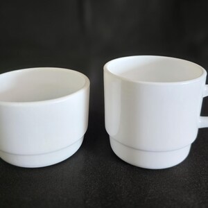 May include: Two white ceramic cups, one with a handle and the other without. Both cups have a simple, modern design.