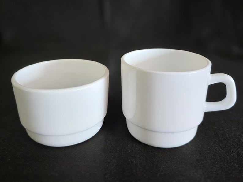 May include: Two white ceramic cups, one with a handle and the other without. Both cups have a simple, modern design.