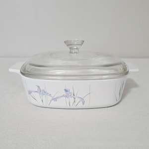 May include: White rectangular casserole dish with a clear glass lid. The dish features a floral design with purple and blue irises. The lid has a clear glass handle and the dish has two white handles.