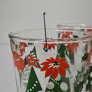 May include: Clear glass drinking glasses with a festive Christmas design. The glasses feature red poinsettias, green Christmas trees, and white dots. The design is repeated around the glass.