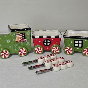 May include: A festive Christmas train set with three ceramic cars in green and red, decorated with snowflakes and candy cane wheels. Includes a set of candy cane-topped spreaders.
