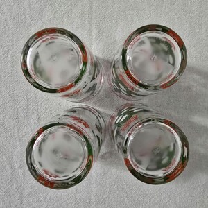 May include: Four clear drinking glasses with a red, white, and green design around the rim. The glasses are arranged in a square, with the bottoms facing the viewer. The design includes what appears to be a stylized floral pattern.
