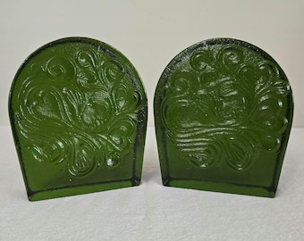 May include: A pair of dark green bookends with a rounded top edge and a raised, swirling embossed pattern across the front surface. The objects have a smooth, glossy finish and a solid, heavy appearance, designed to support books upright.