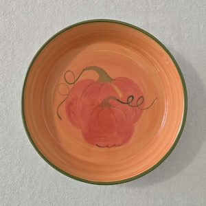 May include: Round orange ceramic plate with a hand-painted pumpkin design. The pumpkin is a reddish-orange colour with green vines. The rim of the plate is a darker green.