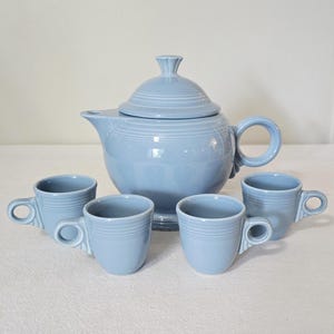 May include: A light blue ceramic tea set featuring a teapot with a lid and four matching teacups. The teapot has a rounded body, a curved handle, and a spout. The teacups have small handles and a simple design. The set is ideal for serving tea.