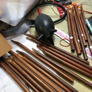 May include: A close-up of a collection of brown wooden calligraphy nibs. The nibs are arranged on a white surface and some are laying on a brown surface. The nibs have a variety of shapes and sizes.
