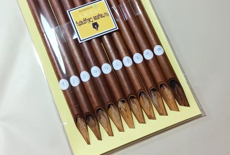 May include: A set of ten brown bamboo calligraphy pens with numbered labels. The pens are arranged in a row, with the tips facing the viewer. The pens are in a clear plastic package with a yellow background.