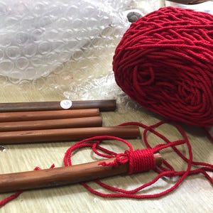 May include: Red rope wrapped around wooden dowels. The rope is tied in a knot and the dowels are arranged in a stack.