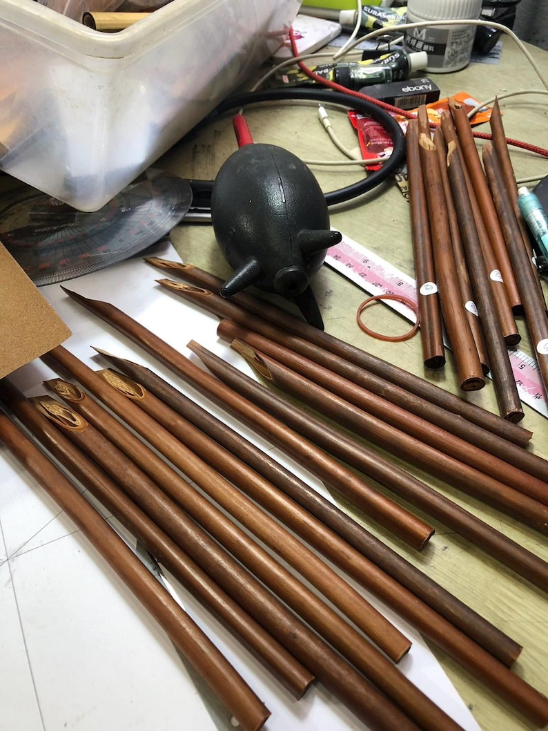 May include: A close-up of a group of brown wooden calligraphy pens with pointed tips. The pens are arranged in a fan shape on a white surface.