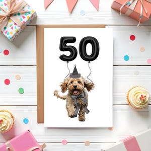 Op de afbeelding: Verjaardagskaart met een cartoonhond met een feesthoedje en een strikje, met het nummer 50 als zwarte ballonletters. De kaart is omgeven door cadeaus, cupcakes en confetti.