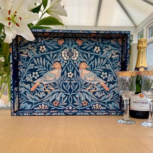 May include: A rectangular serving tray featuring a dark blue background with a repeating pattern of two birds facing each other, surrounded by intricate light blue and peach-coloured floral and leaf motifs. The tray has raised edges and a flat base.