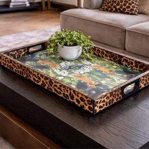May include: A rectangular serving tray featuring a bold leopard print pattern on the exterior sides and handles. The interior base displays a detailed botanical illustration with green foliage and floral elements, holding a small white plant pot.