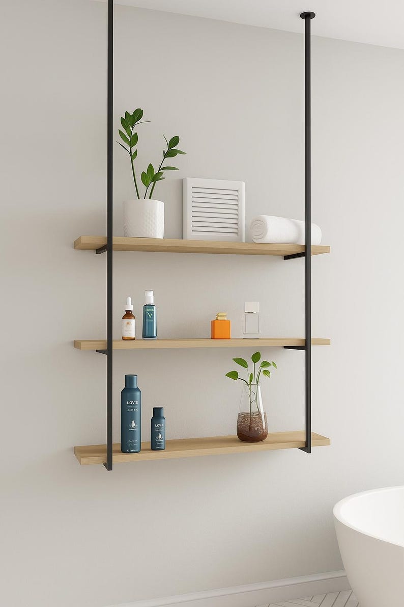 May include: A three-tiered, hanging bathroom shelf with black metal supports and light wood shelves. The shelves hold various toiletries, plants in white and glass vases, and a rolled white towel. The design is modern and minimalist.