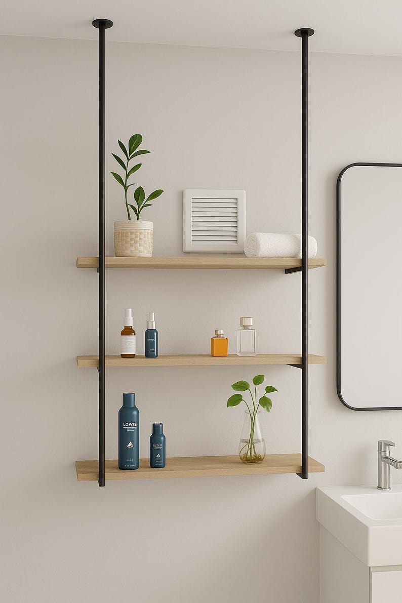 May include: A three-tiered wooden shelf unit with black metal supports, holding various bathroom products and decorative items. The shelves display skincare bottles, a small plant, a rolled towel, and a decorative square. The unit is mounted against a neutral wall.