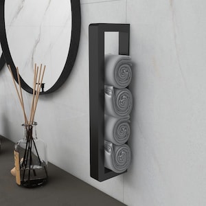 May include: Black metal towel rack with four gray towels rolled up and stacked on the rack. The rack is mounted to a white tiled wall.