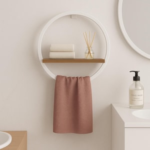 May include: A modern bathroom shelf with a white circular frame, a wooden shelf, and a hanging towel. The shelf holds two folded white towels and a glass diffuser. A pink towel hangs below. A bottle of hand wash is on the counter.