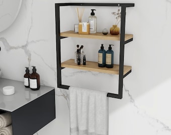 May include: A black metal and wood bathroom shelf with three levels. The top two shelves hold bottles, jars, and decorative items. A gray towel hangs from the bottom. The shelf is mounted on a white marble-patterned wall.