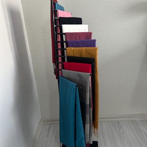 May include: A black metal stand with multiple shelves displaying a variety of colorful scarves. The scarves are arranged in a cascading pattern, with the bottom scarf being a teal blue.