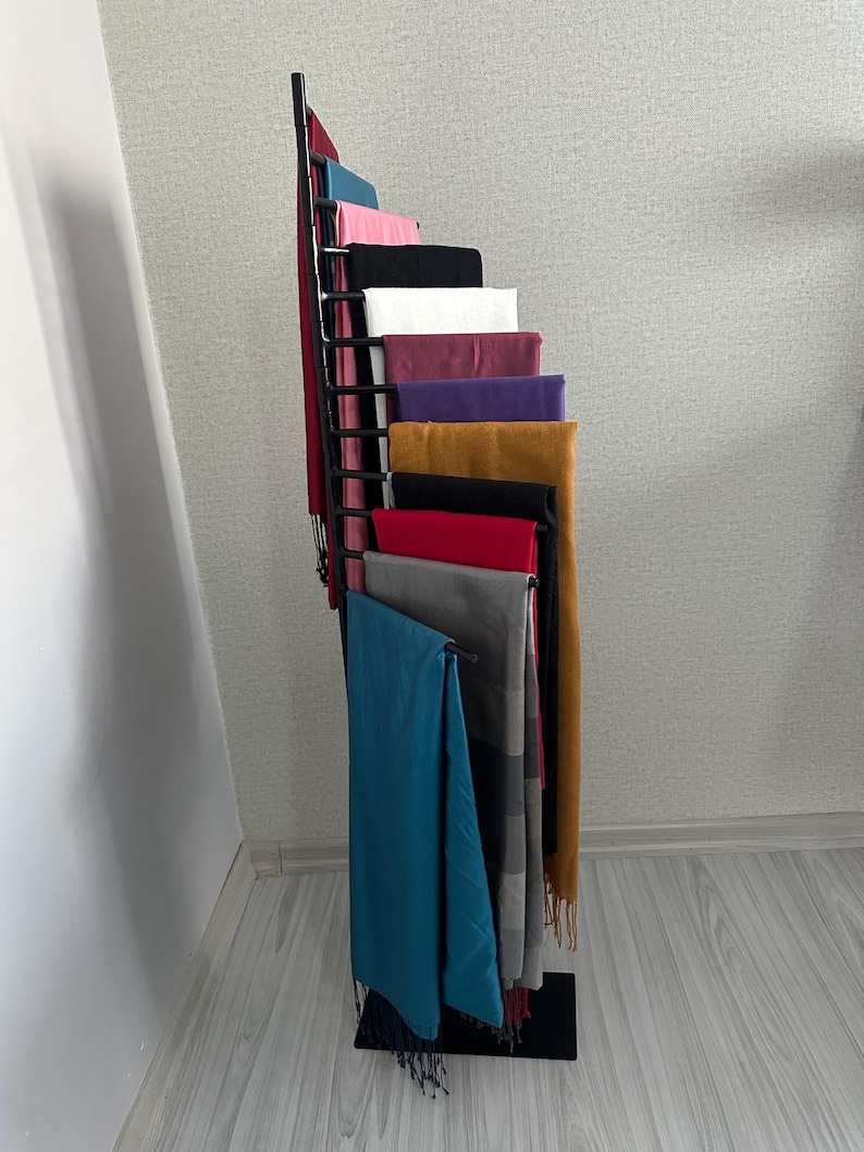 May include: A black metal stand with multiple shelves displaying a variety of colorful scarves. The scarves are arranged in a cascading pattern, with the bottom scarf being a teal blue.