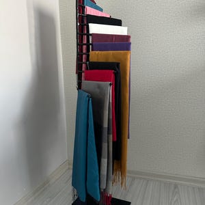 May include: A black metal stand with multiple tiers for displaying scarves. The stand is filled with a variety of colorful scarves, including teal, red, black, white, and purple.