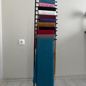 May include: A black metal stand with multiple tiers for displaying scarves. The stand is filled with a variety of colorful scarves, including teal, red, gray, mustard yellow, purple, and pink.