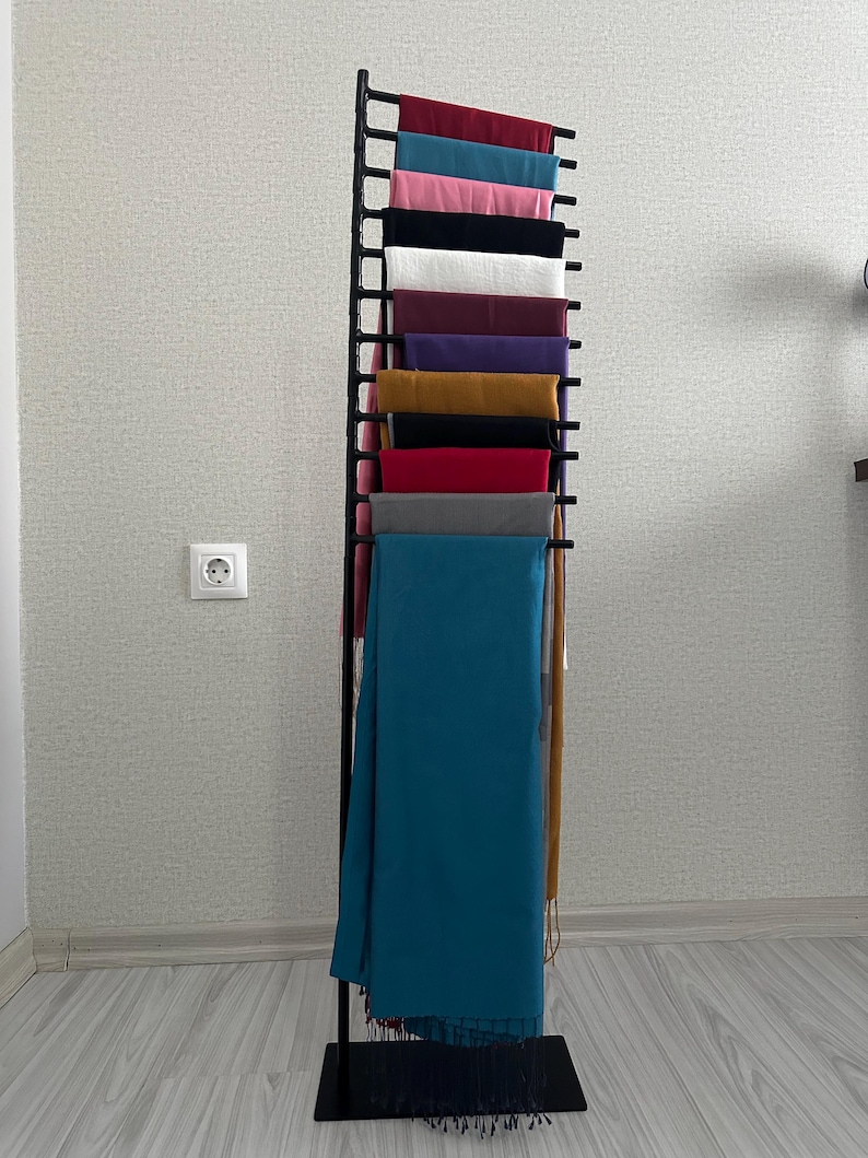 May include: A black metal stand with multiple tiers for displaying scarves. The stand is filled with a variety of colorful scarves, including teal, red, gray, mustard yellow, purple, and pink.