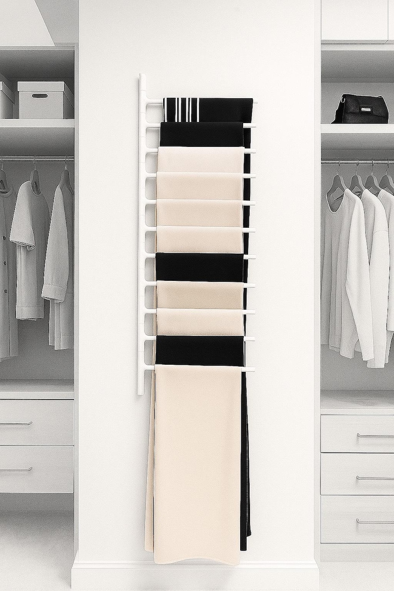 May include: A white scarf rack displaying black and cream-coloured scarves. The rack is mounted on a white wall, with wardrobes on either side. The scarves are neatly arranged, demonstrating a minimalist design aesthetic.