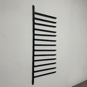 May include: A black metal wall-mounted rack with several horizontal bars. The rack is designed for storage and is fixed to a white wall. The design is minimalist and modern, suitable for various storage needs.