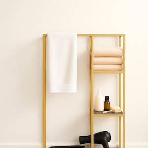 May include: A gold metal bathroom organizer with a white towel, beige towels, and toiletries. The organizer has shelves for storage and a section for a hair dryer and flat iron.