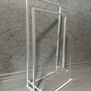 May include: White metal stand with three tiers, featuring a silhouette of a mosque with minarets. The stand is designed for displaying items or as a decorative piece.