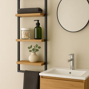 Peut inclure: Étagère de salle de bain moderne avec cadre en métal noir et trois étagères en bois. Les étagères contiennent une serviette grise, un bocal en verre, un distributeur de savon vert et un petit vase blanc avec de la verdure. Un miroir rond et un meuble-vasque en bois sont également visibles.