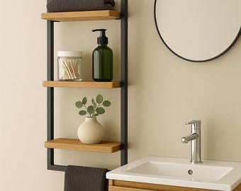 May include: A modern bathroom shelf unit with a black metal frame and three wooden shelves. The shelves hold a gray towel, a glass jar, a green soap dispenser, and a small white vase with greenery. A round mirror and a wooden vanity are also visible.