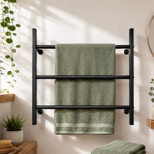 May include: A matte black metal towel rack with three horizontal bars mounted on a wall. A sage green bath towel is draped over the middle and top bars, hanging down to cover the bottom bar. The rack features a simple, clean-lined design.