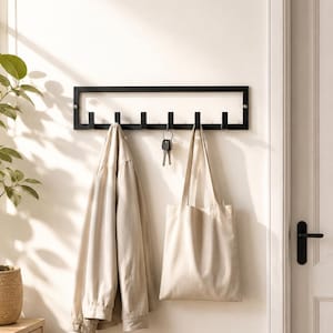 May include: A rectangular black metal wall-mounted coat rack featuring six evenly spaced hooks. A beige jacket and a beige canvas tote bag are hanging from the hooks, along with a set of silver keys suspended from the center hook on the rack.