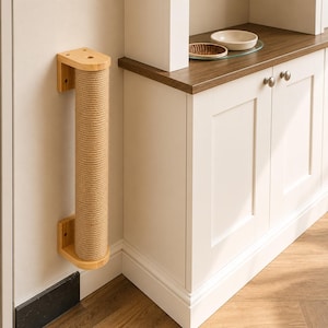 May include: A wall-mounted cat scratching post. The post is made of a natural-colored, tightly wound rope wrapped around a wooden cylinder. The wooden base and top are light-colored, and the post is mounted on a white wall.