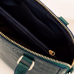 a close-up view of a green leather handbag with a zipper and a gold-colored metal clasp.