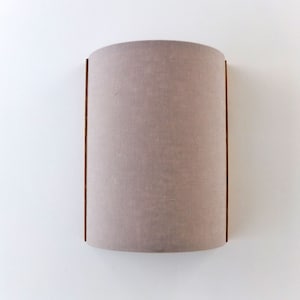 Op de afbeelding: Een gebogen wandlamp met een lichtbeige stoffen kap en houten afwerking.