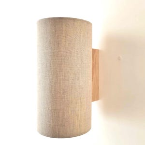 Könnte beinhalten: Eine Wandleuchte mit einem zylindrischen Leinen-Schirm und einem Holzsockel.