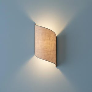Peut inclure: Applique murale incurvée avec un abat-jour en tissu beige. La lumière diffuse une lueur chaude sur le mur bleu clair, créant une ambiance douce et accueillante. Design moderne et minimaliste.