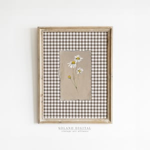 May include: A framed print of a watercolor painting of white daisies with yellow centers on a brown gingham background. The frame is a light wood color. The print is titled "SOLANO DIGITAL vintage art alliance".