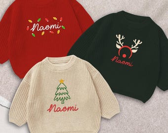 May include: Three Christmas-themed sweaters in red, green, and cream. Each sweater has the name "Naomi" embroidered in cursive. The red sweater features colorful lights, the green sweater has reindeer antlers, and the cream sweater has a Christmas tree.