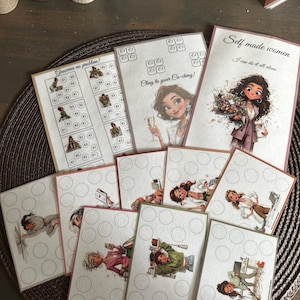 Op de afbeelding: Een verzameling bedrukte spaarchallenge-kaarten met illustraties van vrouwen in diverse situaties. De kaarten bevatten teksten zoals Groceries no problem!, Cling to your Ca-ching! en Self made women, I can do it all alone, naast cirkelvormige vakjes voor het bijhouden van financiële voortgang.