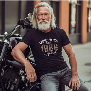 May include: Black t-shirt with the text "LIMITED EDITION MADE IN 1966 Helmut" in white and brown lettering. The shirt is short-sleeved and worn by a person with long white hair and a beard, leaning on a motorcycle.