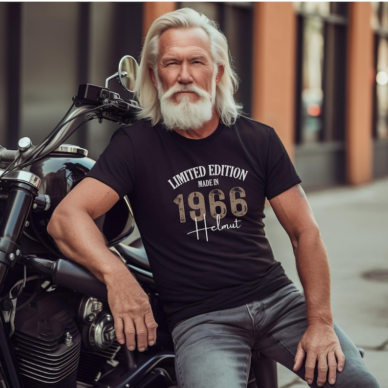 May include: Black t-shirt with the text "LIMITED EDITION MADE IN 1966 Helmut" in white and brown lettering. The shirt is short-sleeved and worn by a person with long white hair and a beard, leaning on a motorcycle.