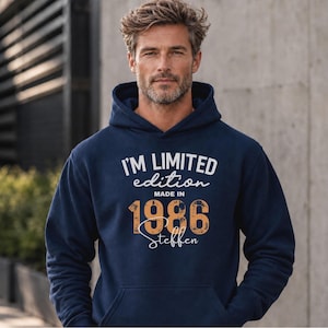 Könnte beinhalten: Ein marineblauer Kapuzenpullover mit weißem und orangefarbenem Text, der I'M LIMITED edition MADE IN 1986 Steffen lautet. Der Hoodie verfügt über eine Kängurutasche auf der Vorderseite und lange Ärmel mit einem Grafikdruck auf der Brust.