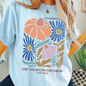 May include: A light blue t-shirt with a floral design and the text "Consider the wildflowers grow Luke 12:27".