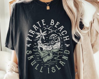 May include: Black t-shirt with a graphic print of a skull with a palm tree and beach umbrella inside. The text around the skull reads "Pirate Beach Skull Island".
